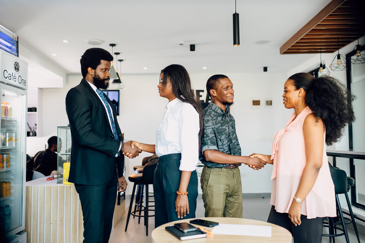 journey Four adults engage in a professional handshake at a cafe in Lagos, Nigeria, showcasing teamwork and collaboration.