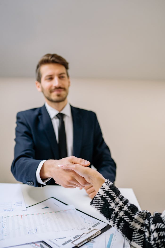 A professional handshake exchanged between a businessperson and client at a desk.